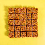 Caramel Cornflake Brownie squares with crunchy malted caramel cornflake topping on a yellow background by Crumbs & Doilies